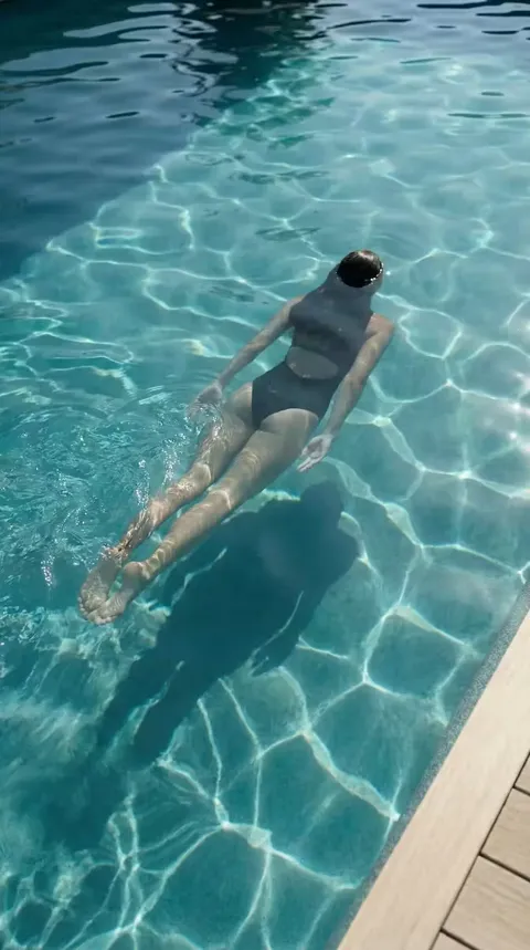 Nageuse en maillot foncé immergée à la surface d'une piscine, eau claire avec reflets prismatiques